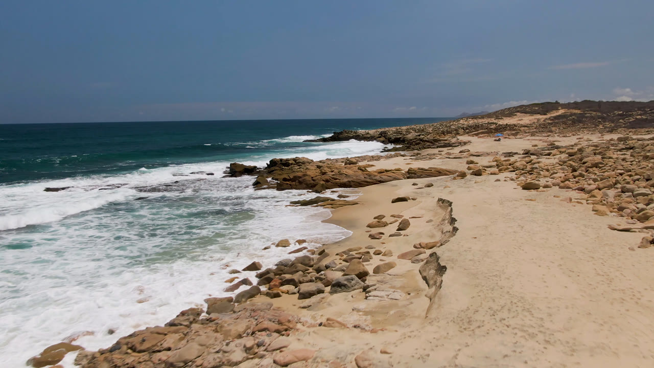Laguna Beach shoreline view with foamy water around foreground rocks, pale sand to the right, and no visible people.