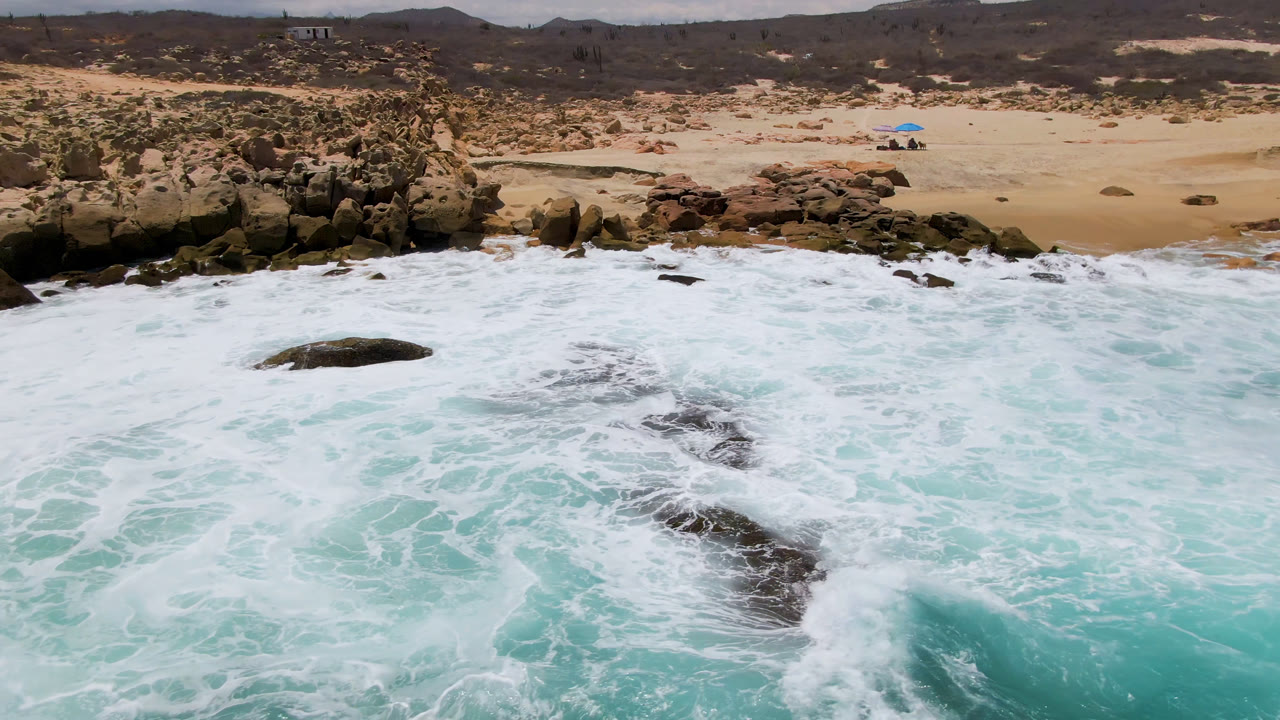 Foamy surf breaking over rocks below a sandy beach