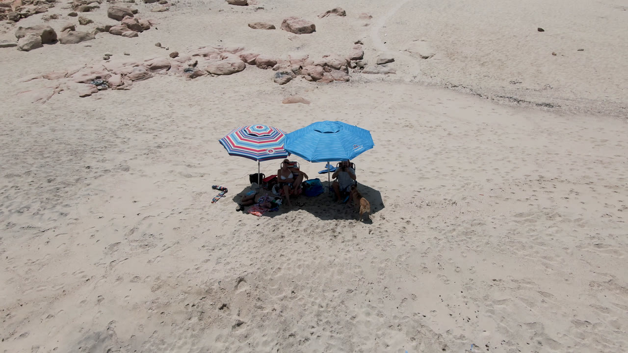 Two beach umbrellas shading people on a sandy beach