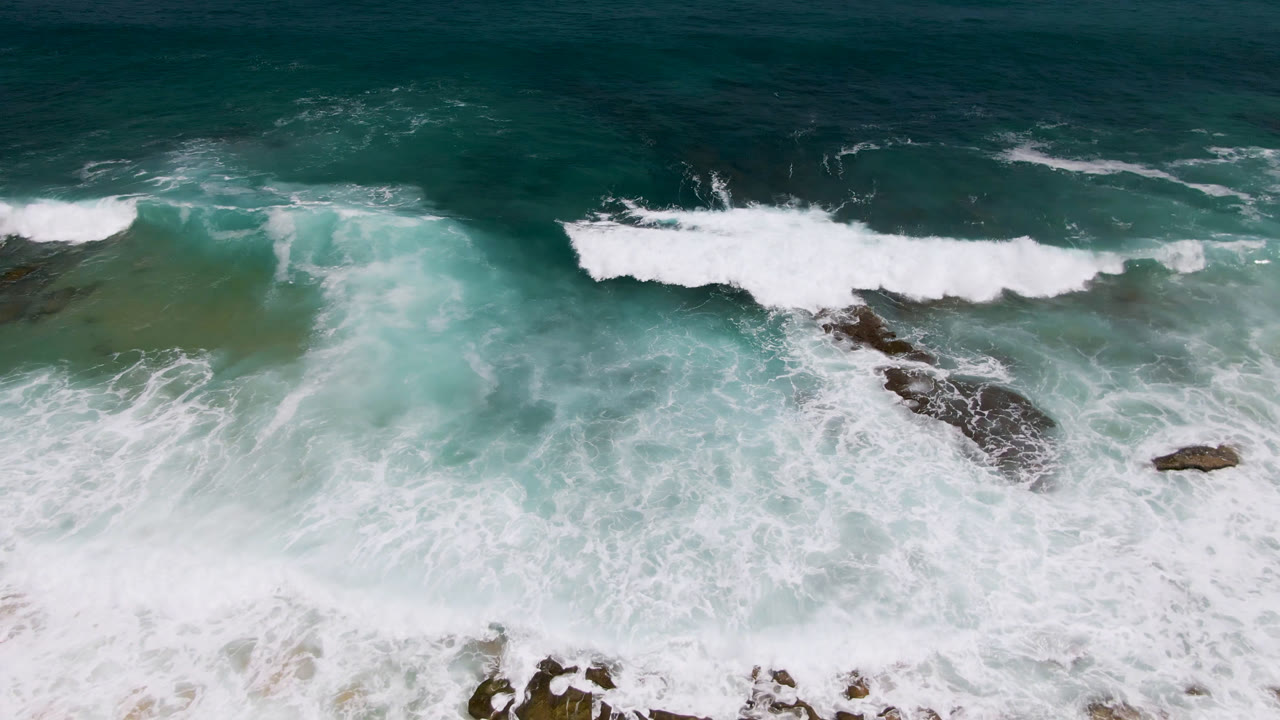 Breaking wave over turquoise water and scattered rocks.