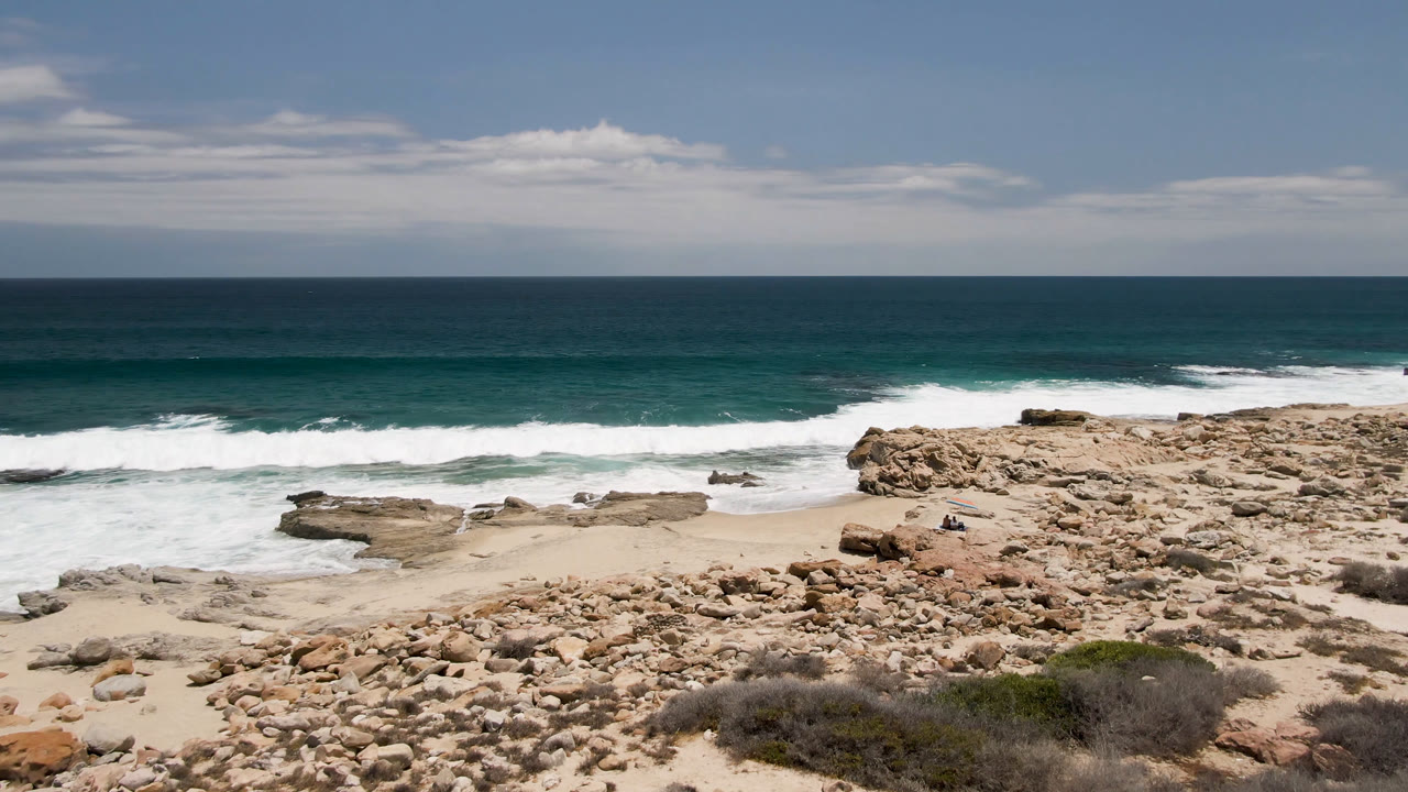 At Laguna Beach in Baja California Sur, Mexico, the rocky right side of the beach stands out while breaking surf spreads across the midground, with no visible people in the frame.