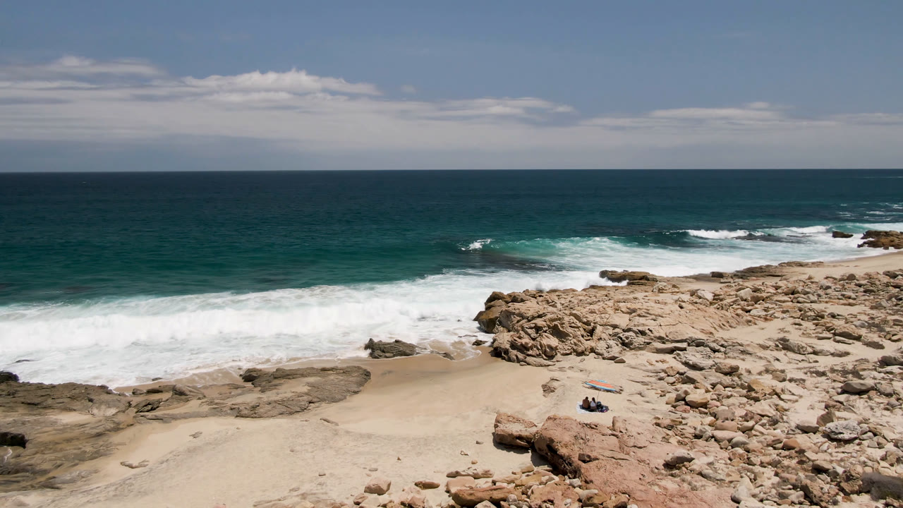 Wide elevated view of waves breaking on a rocky beach with ocean horizon.