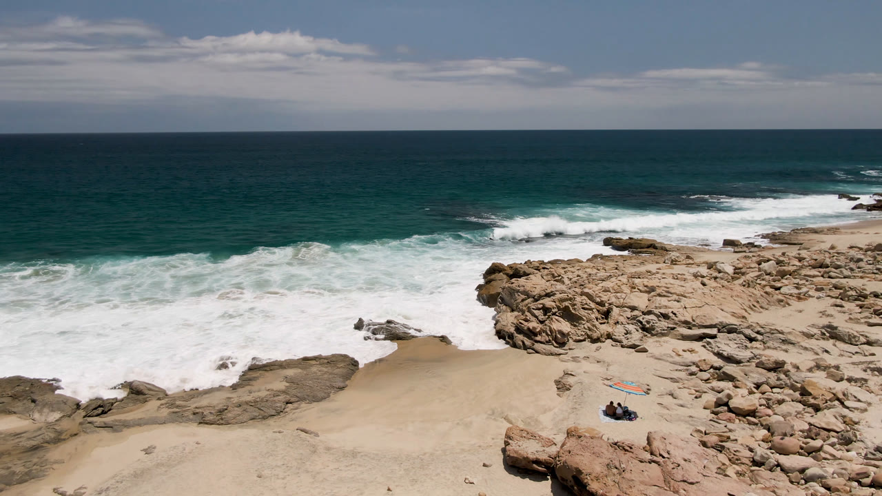 Aerial view of rocky beach, surf, and small people on sand