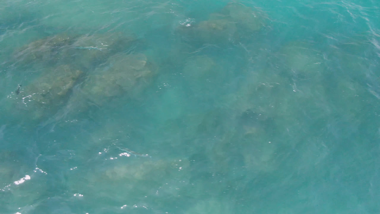 Top-down view of turquoise water over submerged rocks at Laguna Beach, Baja California Sur, with small ripples and no visible people.