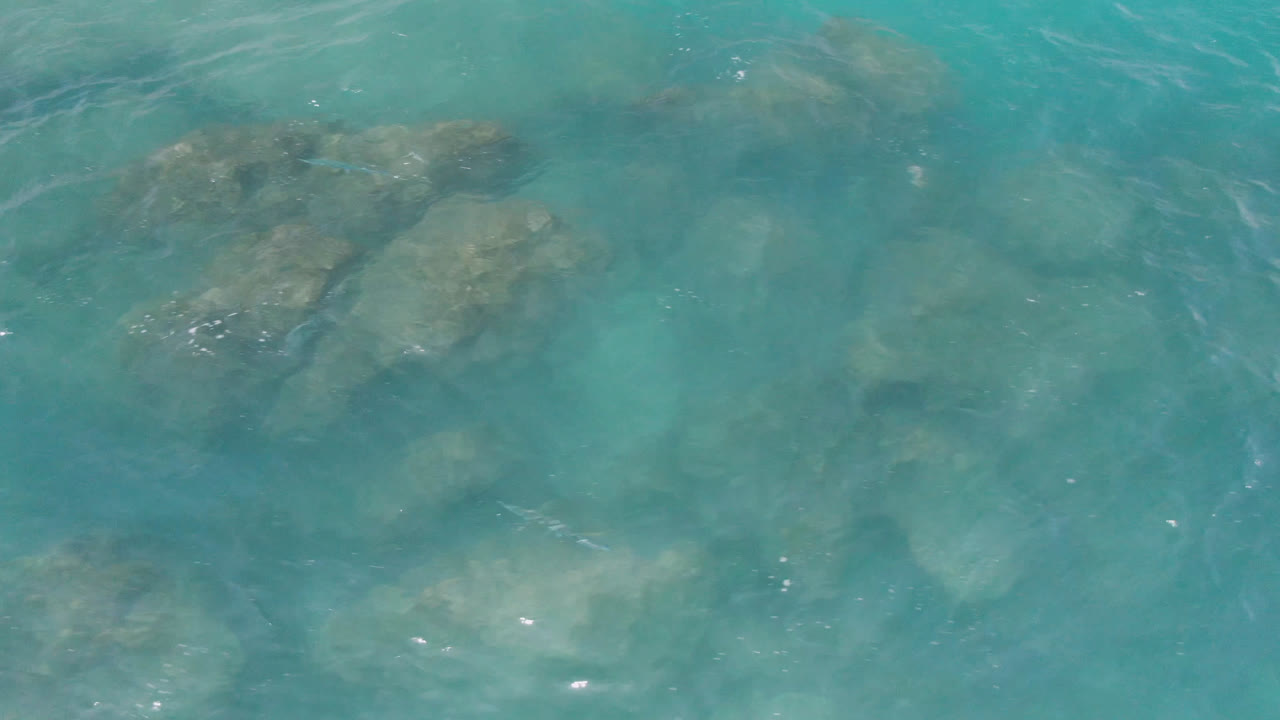 Blue-green water at Laguna Beach, Baja California Sur reveals a central submerged rock shape beneath soft surface motion, with no visible people.
