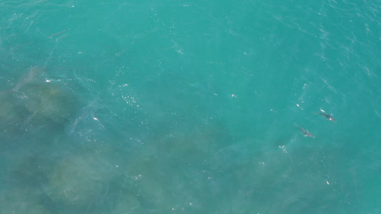 Top-down view of turquoise ocean at Laguna Beach, Baja California Sur, with faint darker underwater patches, white glints, and no visible people.
