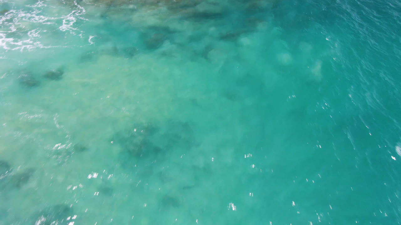 Clear teal ocean surface with foam at the top and scattered dark patches.