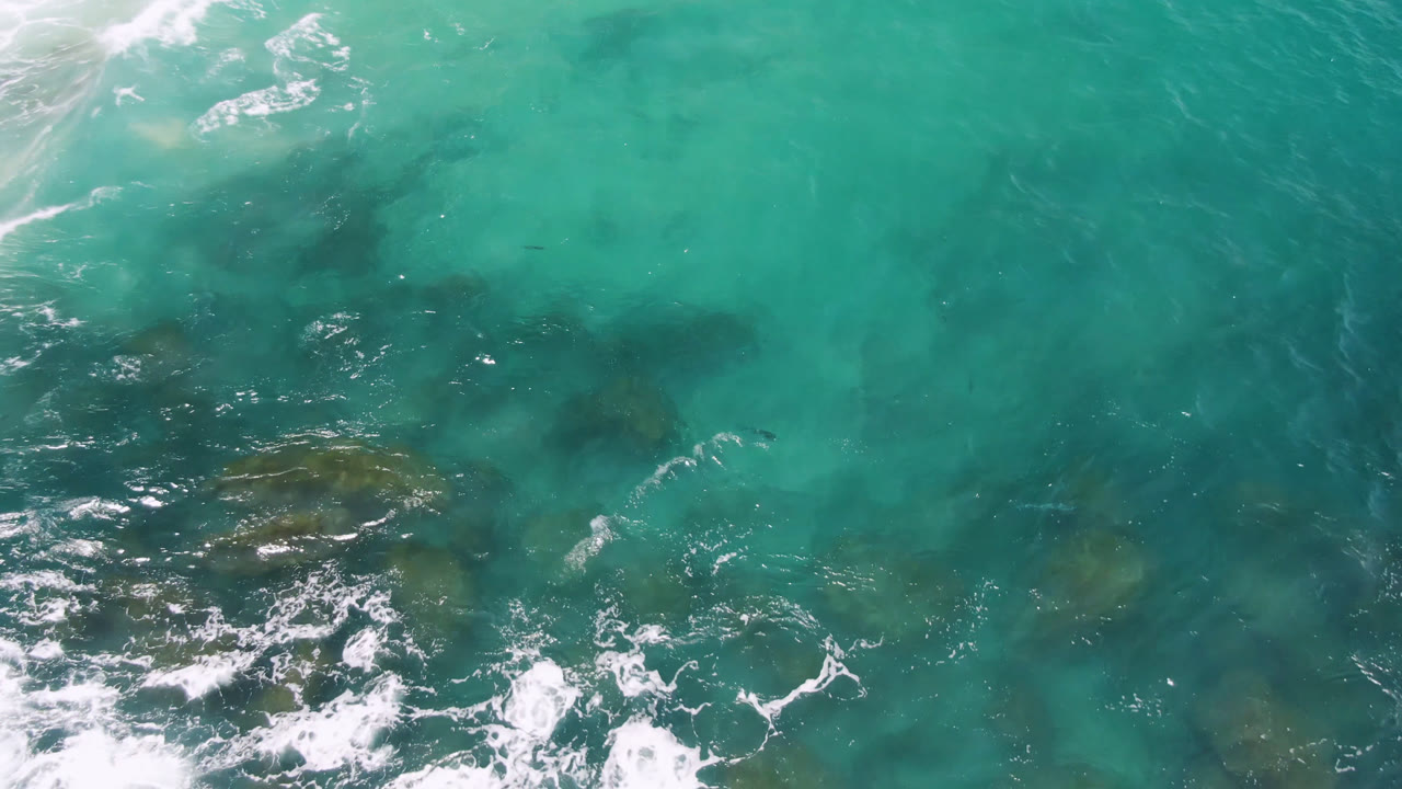 Turquoise ocean surface with larger foam streaks over submerged rocks