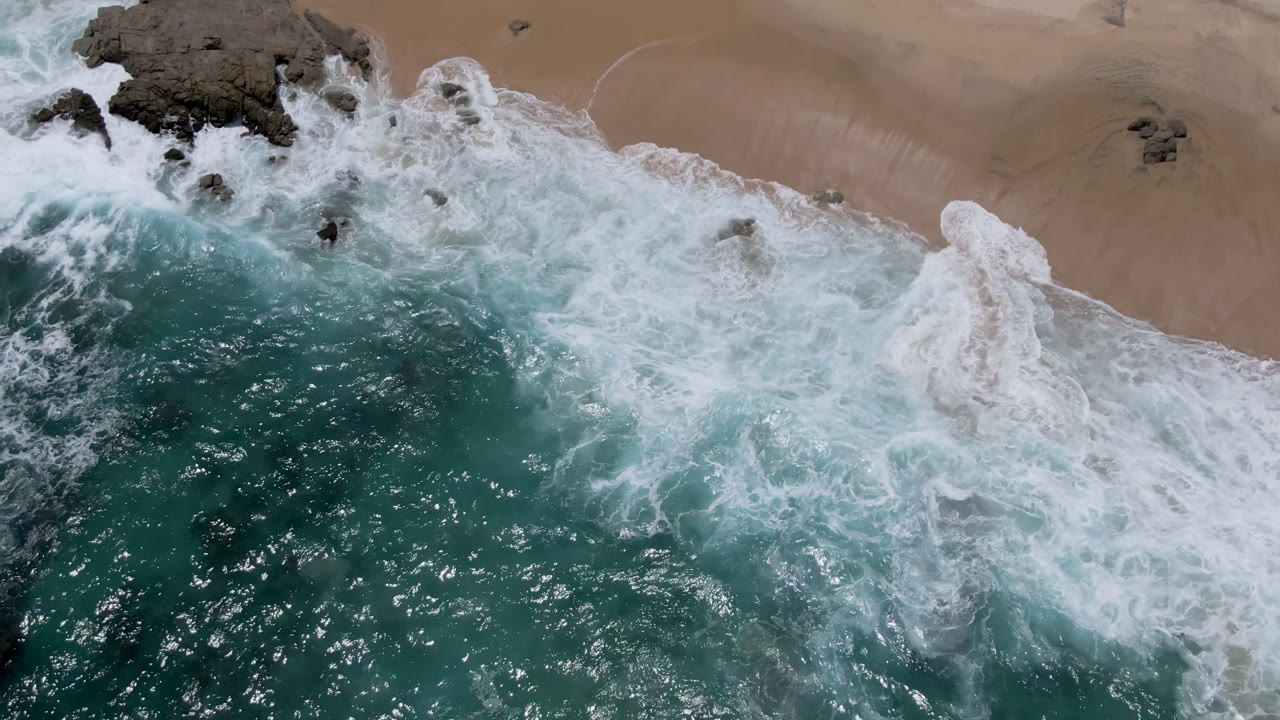 Overhead surf breaking across rocks and sand