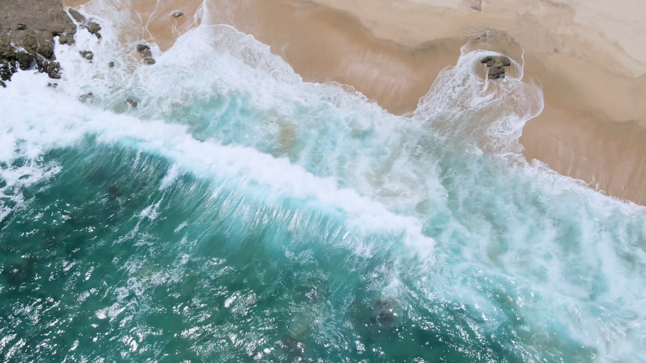 Thick white surf line breaking below a sandy shoreline