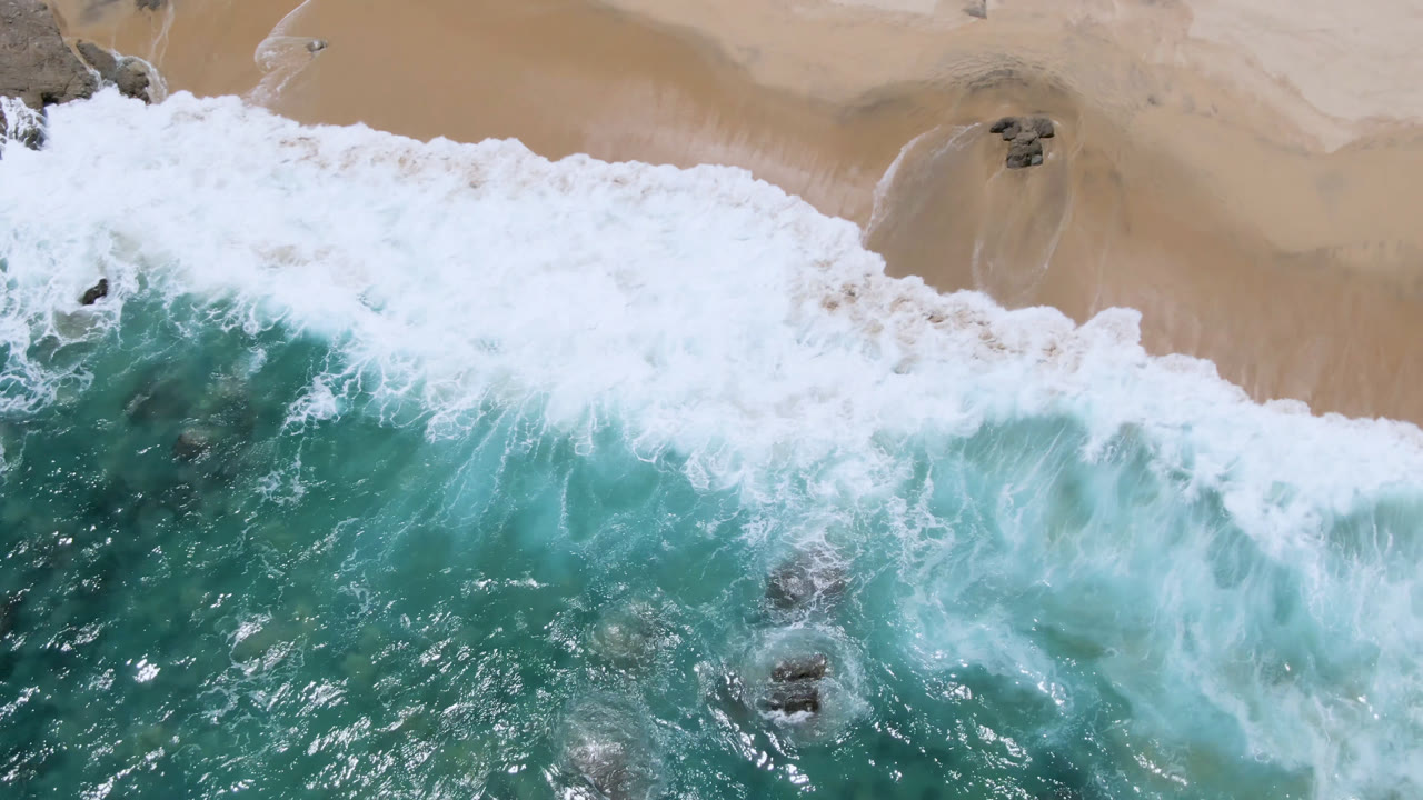 Overhead surf washing onto golden sand with rocks offshore.