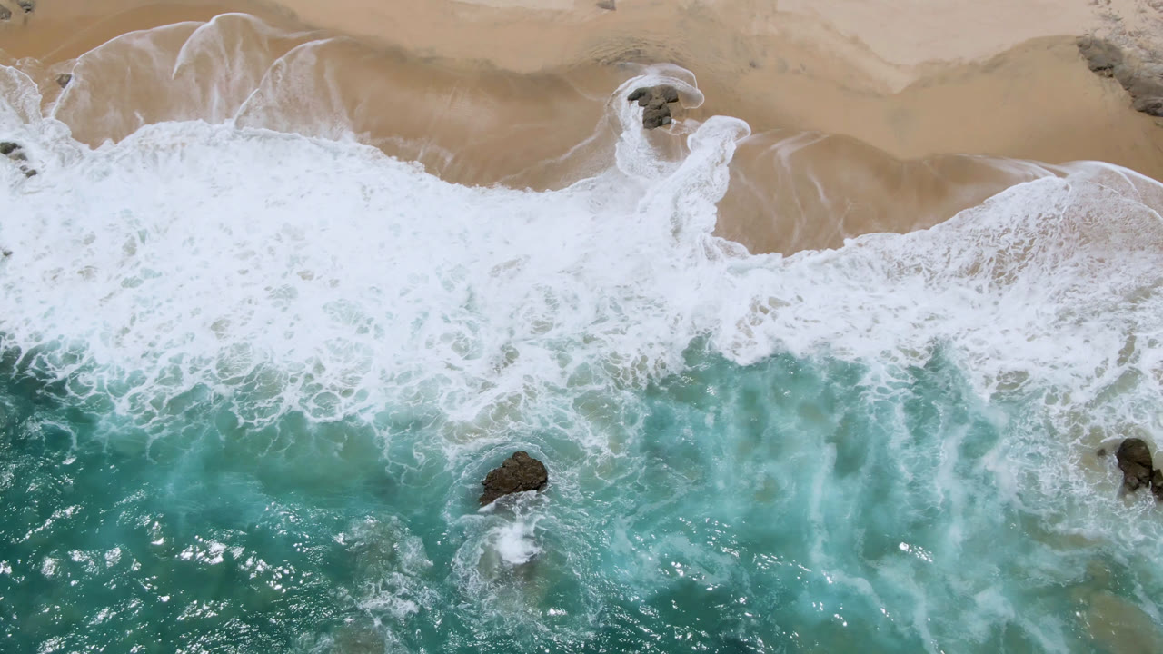 Top-down beach surf with rocks near the foam line