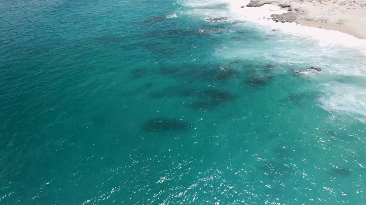 Overhead coastal water with surf, sand, and dark underwater patches.