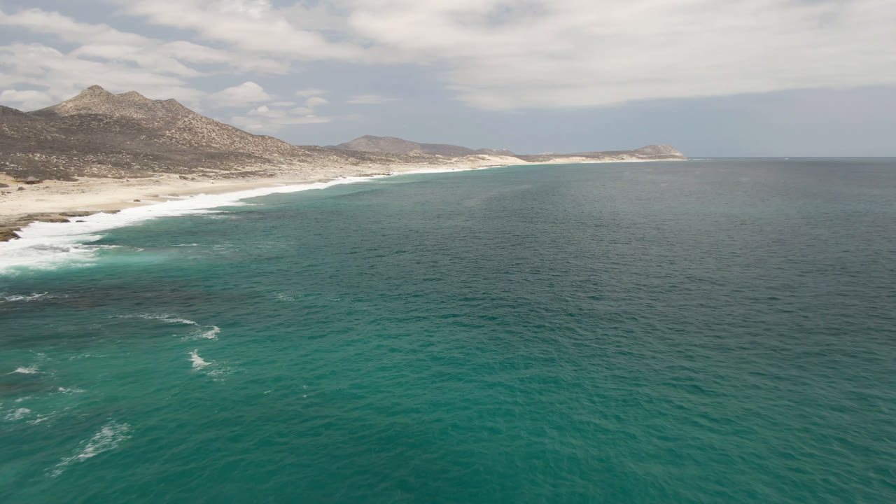 Wide ocean foreground with a mountain-backed beach under clouds.