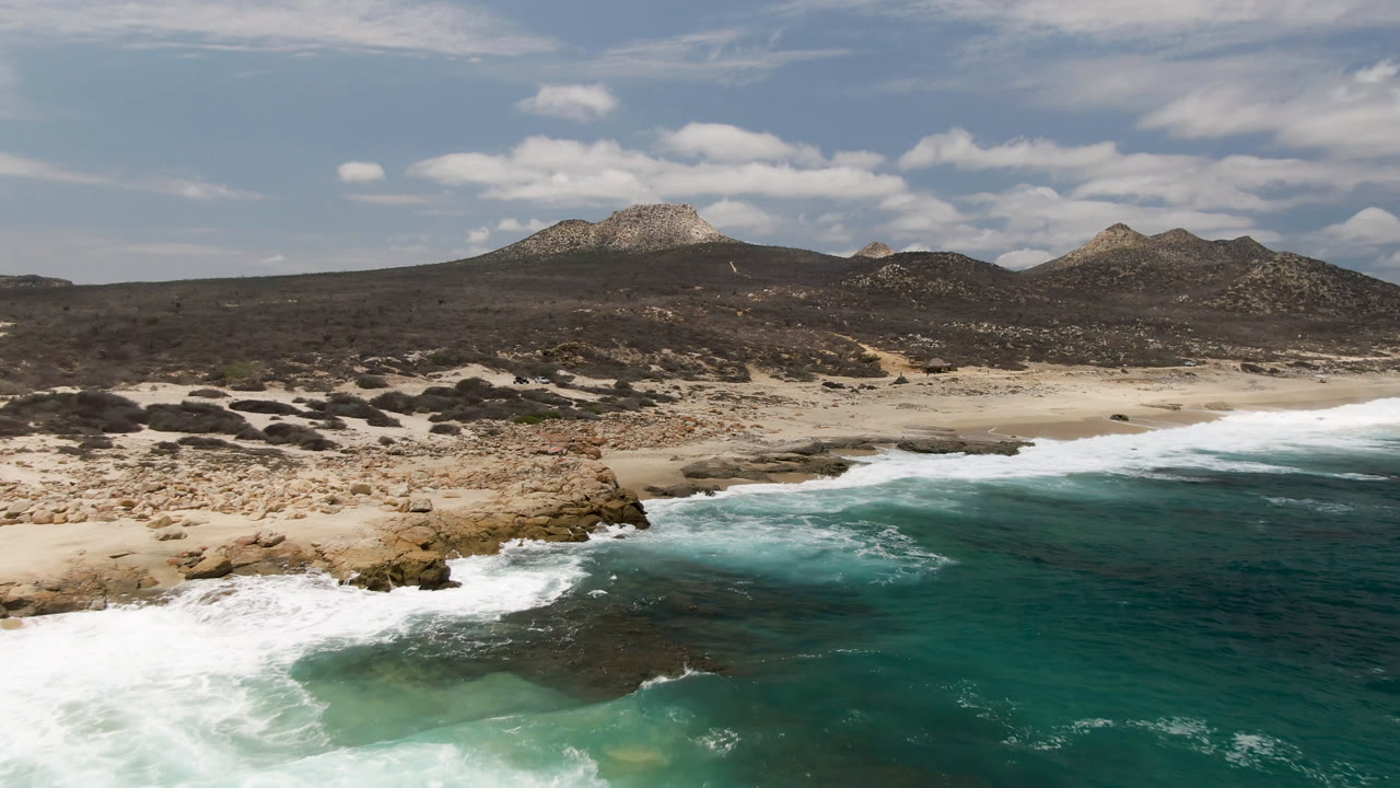 Rocky coast and teal ocean below a bright sky with low mountains in back.