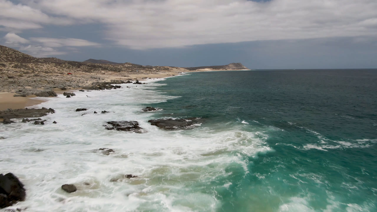 Rocky surf zone with turquoise water and a long empty beach in the background.