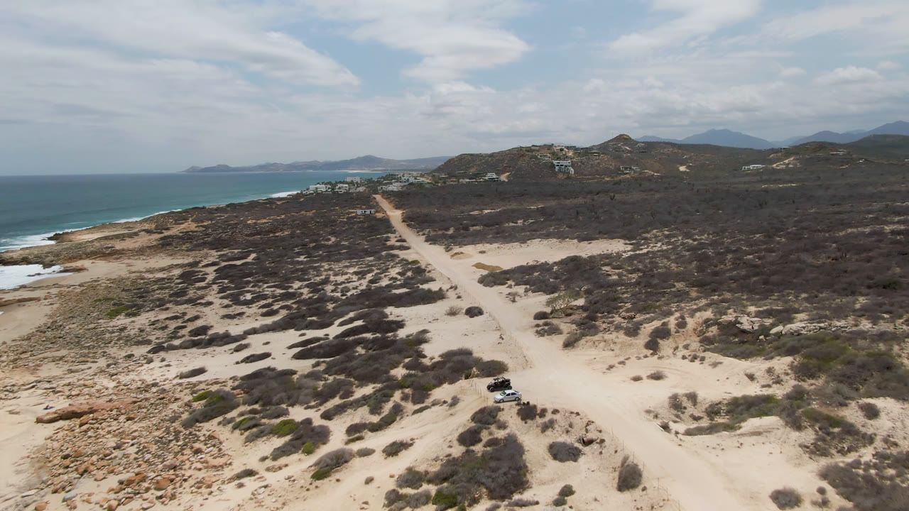 Aerial view of a dirt road near ocean and scrubland.