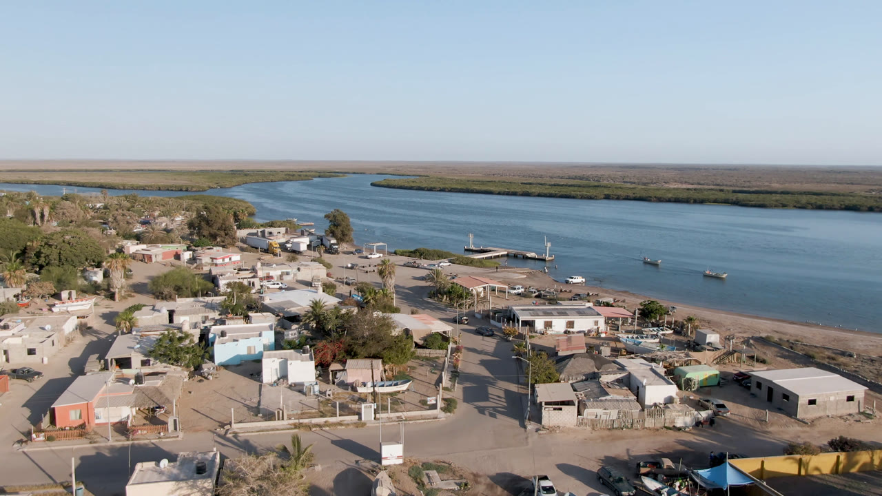 Aerial view of a small riverfront town beside blue water and a sandy shore.