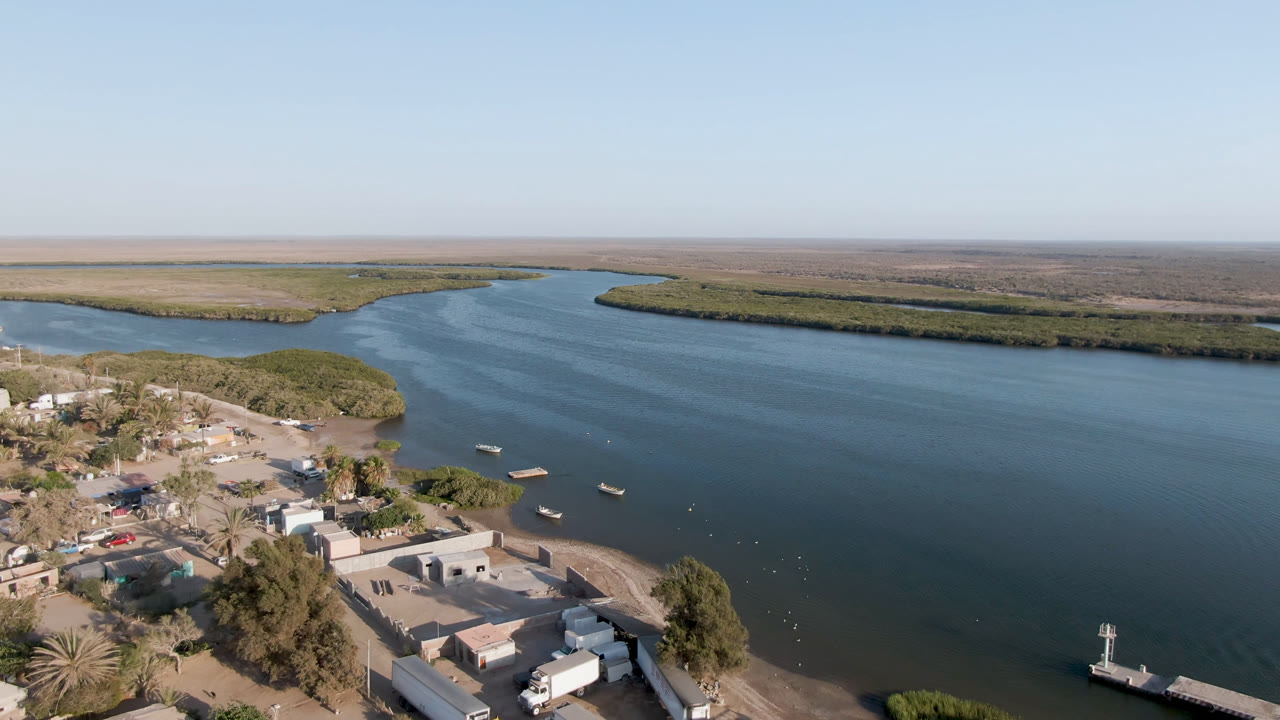 Aerial view in Aldofo Lopez Mateos showing shoreline buildings at lower left, several small boats on the water, vegetated banks across the channel, and no visible people.