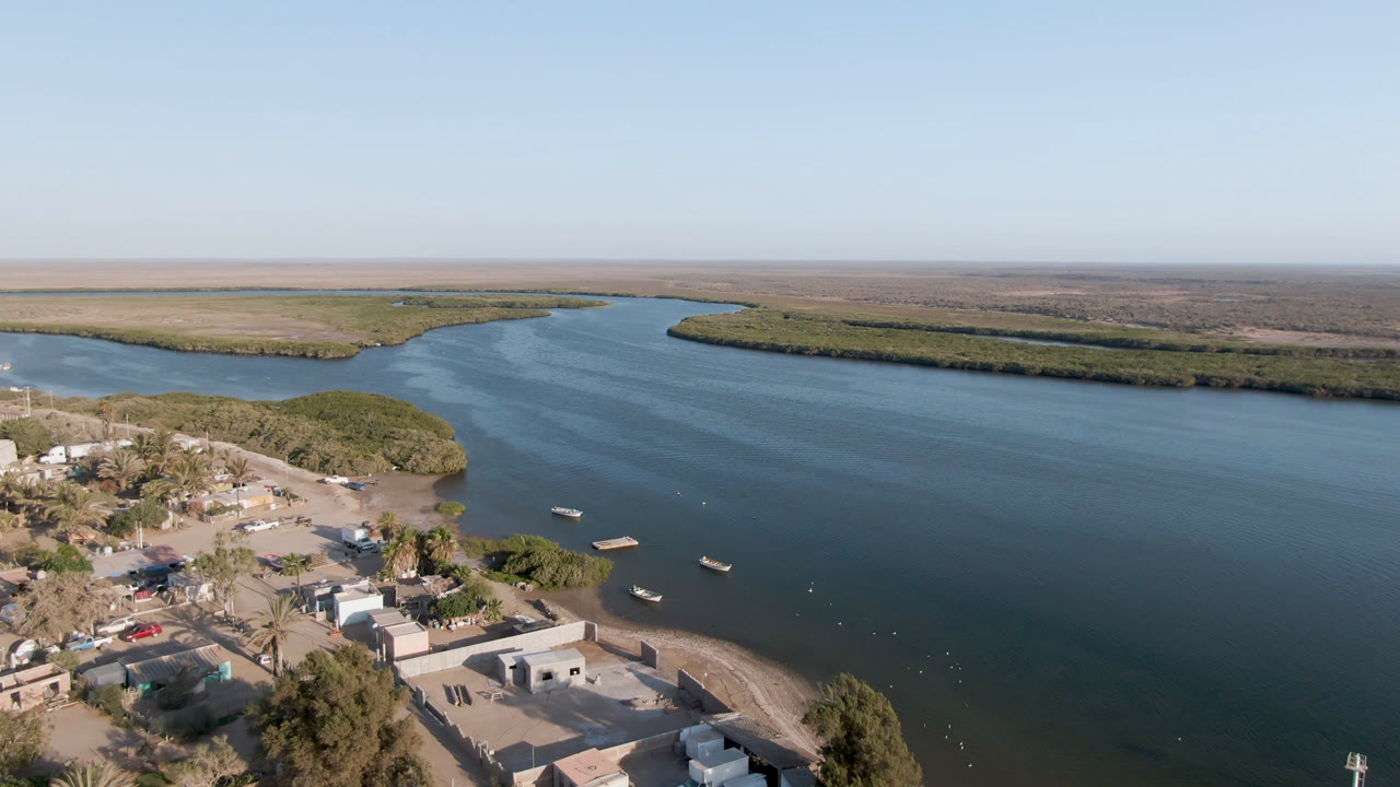Wide aerial of boats on a waterway with town buildings along the near shore.