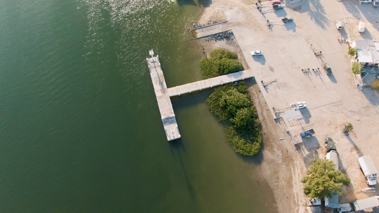 High overhead view of a T-shaped dock beside shoreline trees and parked vehicles.