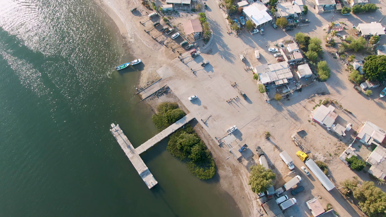 Overhead view of dock, green water, shoreline roads, homes, vehicles, and a small boat.