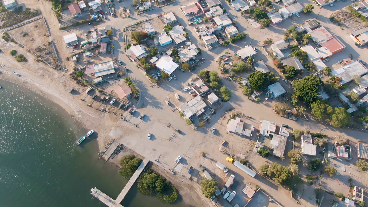 Overhead coastal town with sandy beach, green water, roads, buildings, and boats.