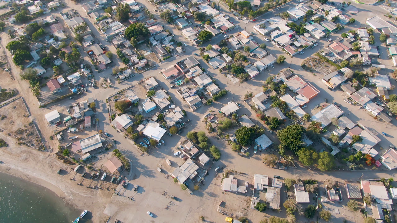 Overhead view of small town houses, dirt roads, trees, and water edge.