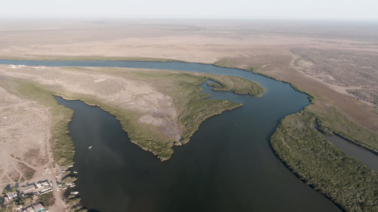 Aerial view over Aldofo Lopez Mateos, Baja California Sur, with dark water channels cutting through pale desert flats, scrub islands, a hazy horizon, and no visible people.