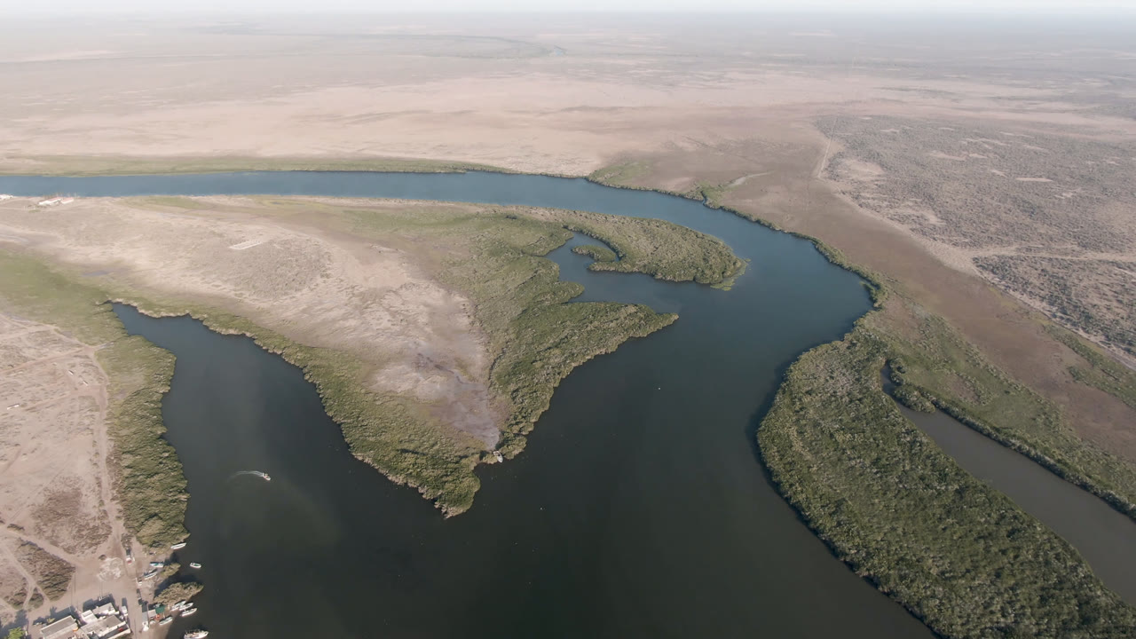 Aerial view of dark water curving around sandy desert flats and green vegetation.