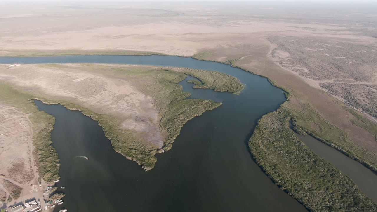 Drone view in Aldofo Lopez Mateos, Baja California Sur, showing a broad bend of dark water bordered by sandbars, scrub vegetation, and open desert, no visible people.