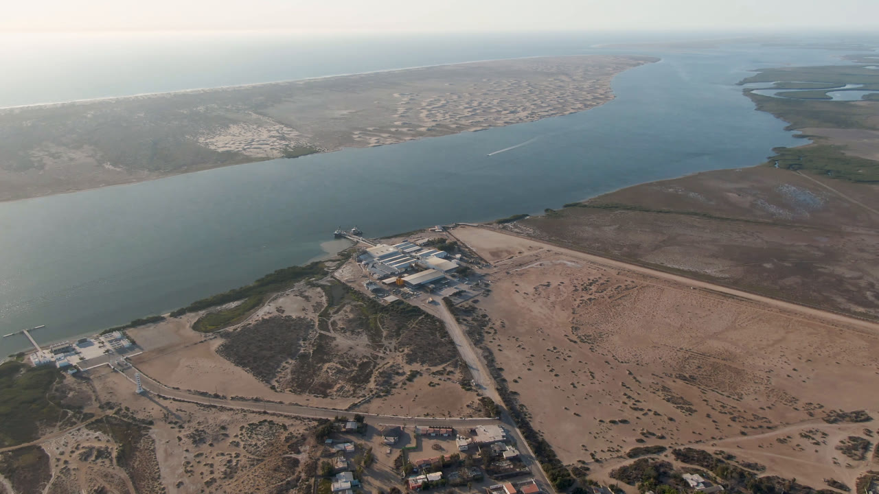 Drone view of a coastal waterway, small shoreline complex, road, and dry land.