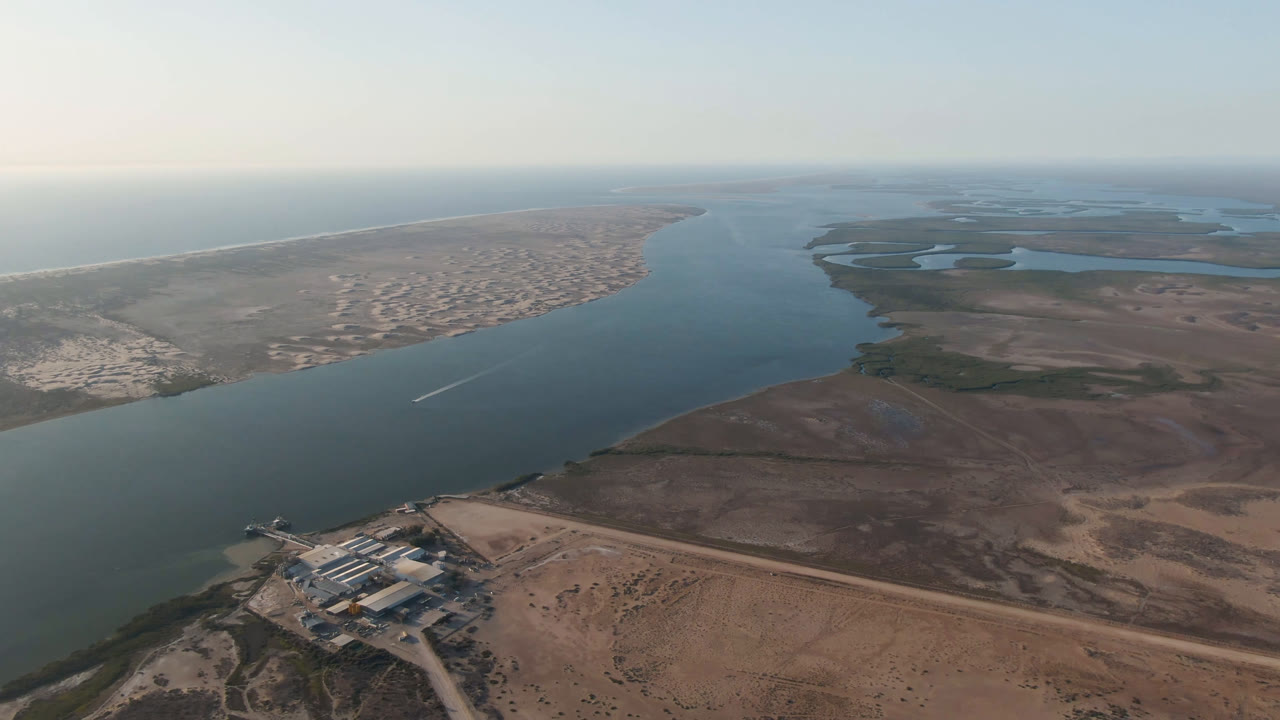 Aerial frame in Aldofo Lopez Mateos, Baja California Sur, with the shoreline buildings lower left, a long sand spit across the channel, and no visible people.