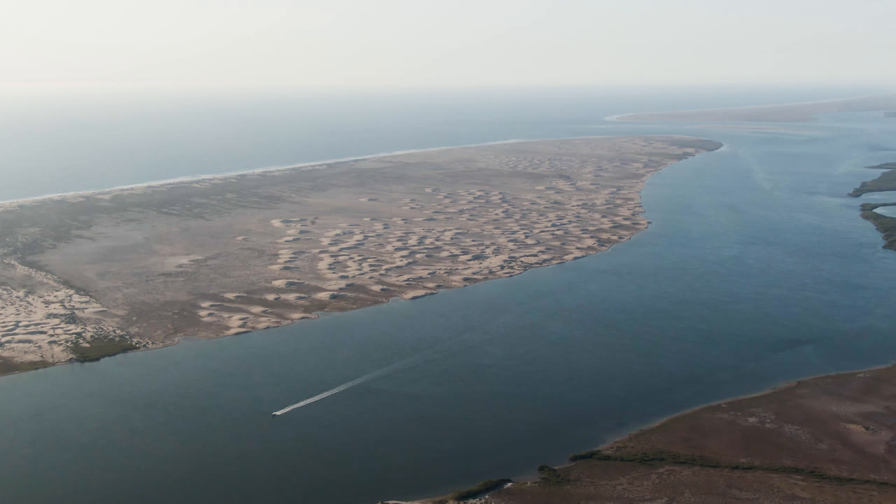 Aerial view over Aldofo Lopez Mateos, Baja California Sur, showing the boat wake slightly farther along the channel, broad sand banks across the middle distance, open water to the right, and no visible people.