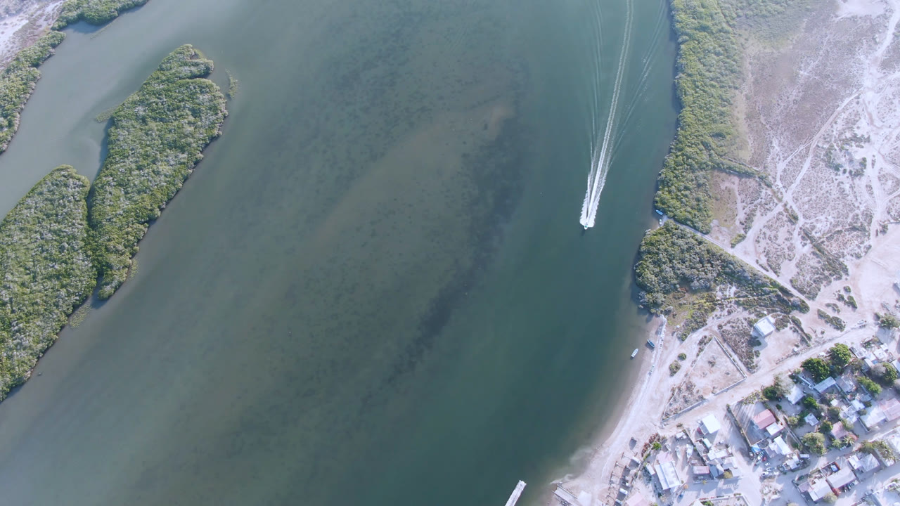 Overhead waterway with a boat wake near sandy shoreline and buildings