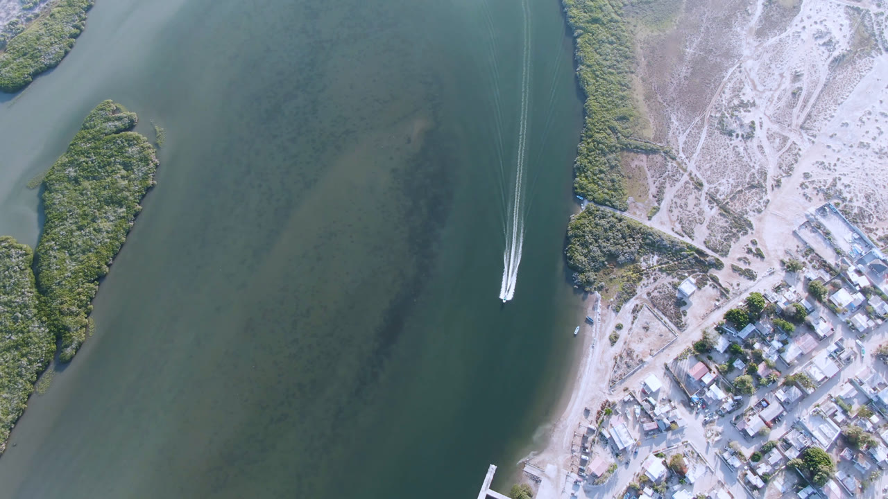 Aerial view in Aldofo Lopez Mateos, Baja California Sur, with the boat wake farther down the channel, open water on the left, shoreline buildings on the right, and no visible people.