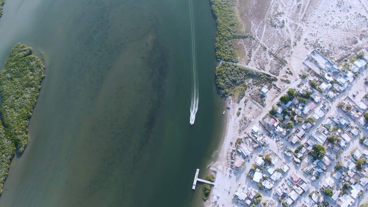 Overhead view of a small boat on green water beside a sandy coastal town.