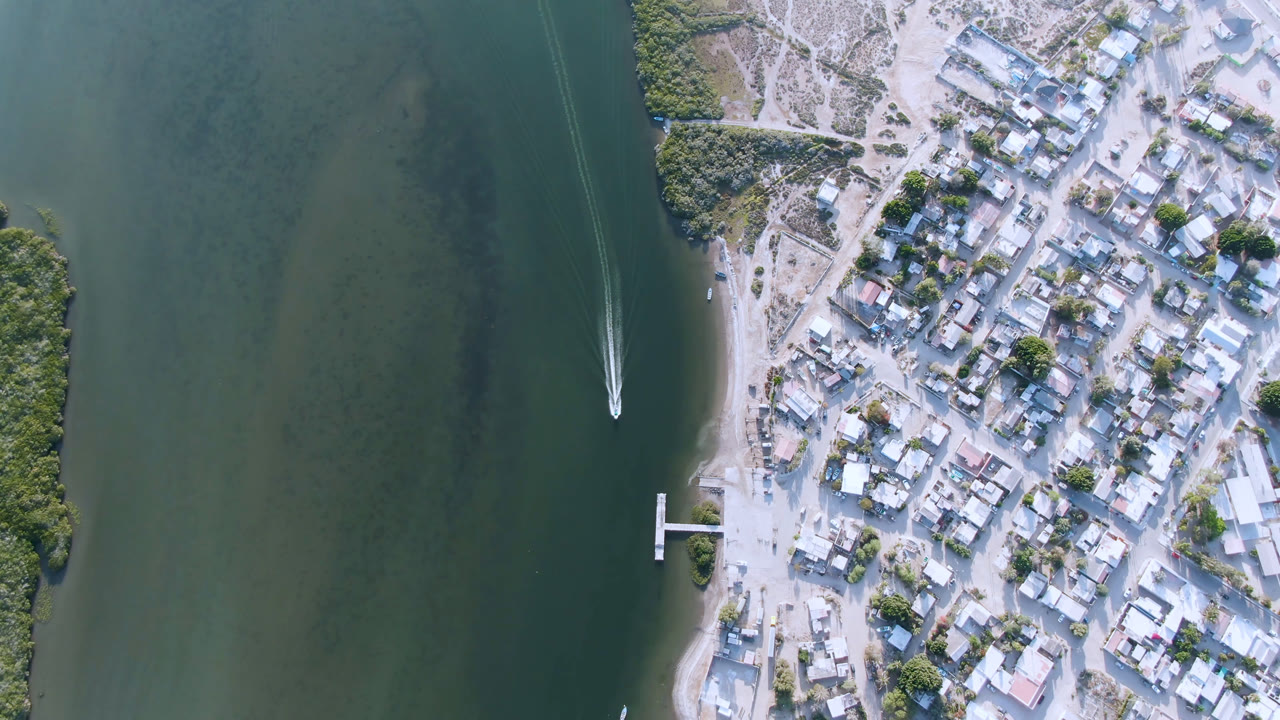 Overhead coastal town beside green water with a boat wake