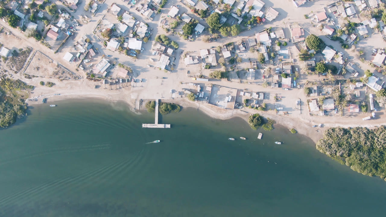 Overhead view of a sandy waterfront town, pier, boats, and green-blue water.