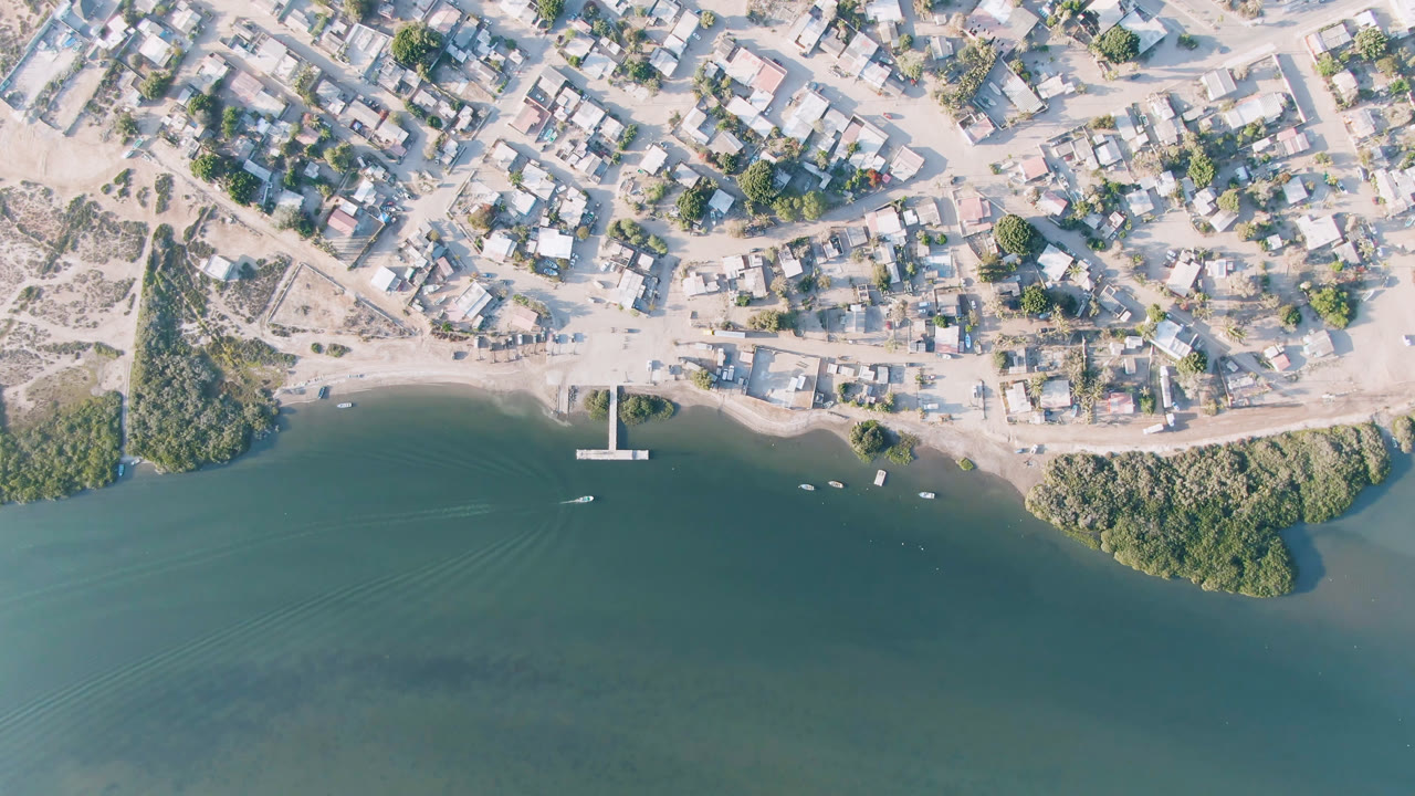 Overhead coastal town beside green-blue water with a small pier and boats.