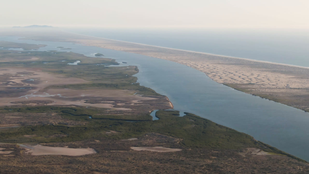 Aerial coastal desert landscape with a channel, inlets, sandbar, and ocean horizon.