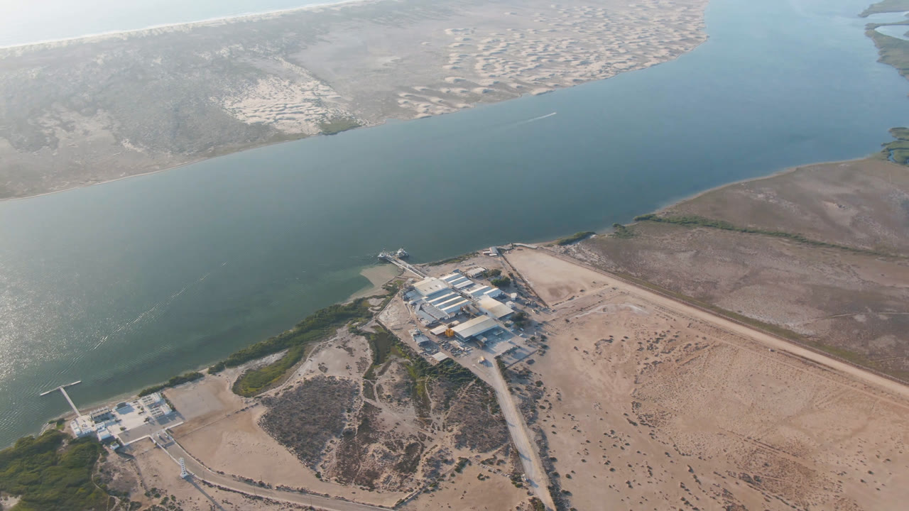 High aerial view of a coastal waterway with buildings and shoreline roads below.