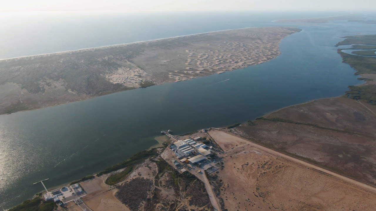 Aerial frame over Aldofo Lopez Mateos, Baja California Sur, with the channel filling the center, delta terrain at right, low shoreline buildings near the bottom, and no visible people.