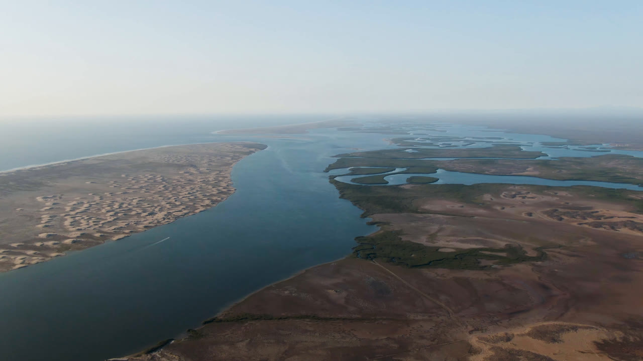 Aldofo Lopez Mateos aerial frame showing the main waterway running toward the horizon, sandy settlement patterns on the left bank, lagoon flats on the right, and no visible people.