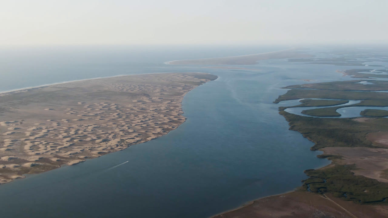 Aerial frame from Aldofo Lopez Mateos with the sandy peninsula filling more of the left side, a broad water channel running through the center, wetland pools on the right, and no visible people.