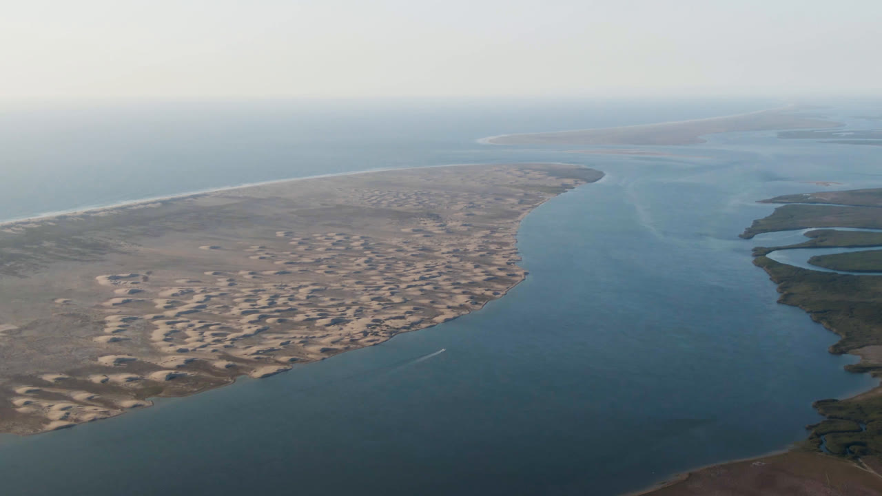 Drone view over coastal water, dunes, and curved beach edge