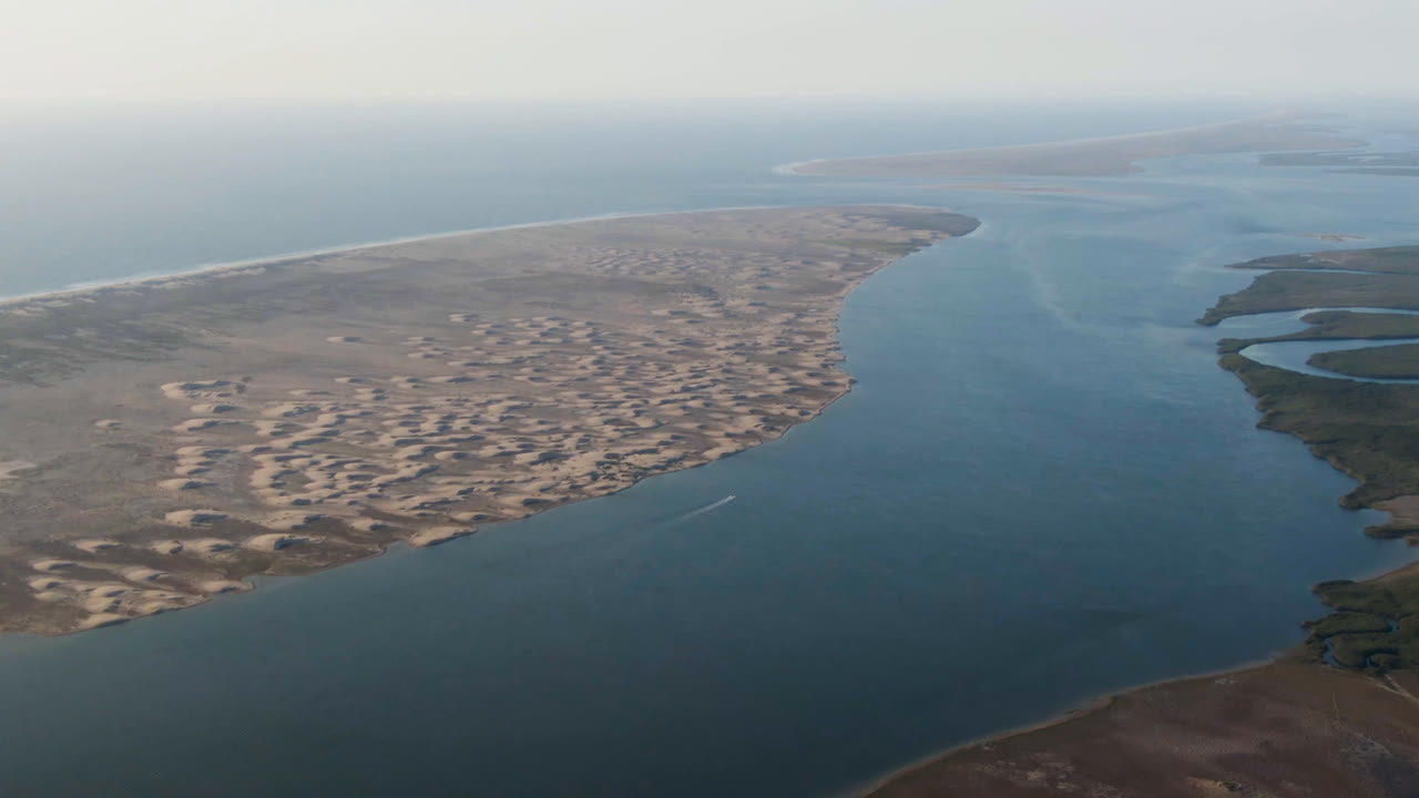 Aerial view over Aldofo Lopez Mateos, Baja California Sur, with a sandy spit dividing blue-green water from darker marsh channels and no visible people.