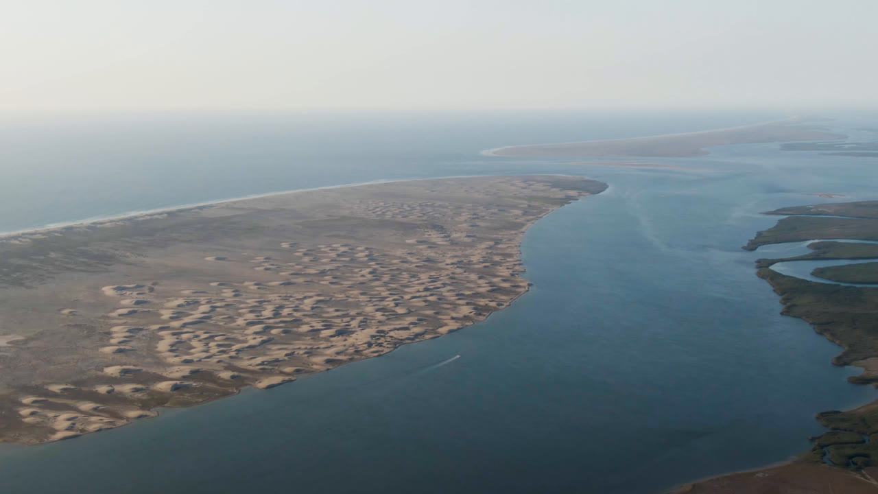 Wide aerial coastline with sandy land on the left and water channels on the right.