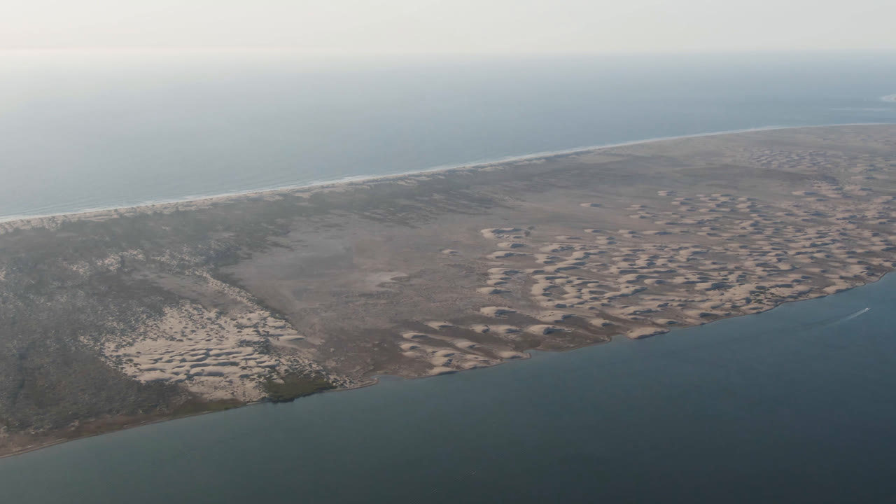 Aerial view in Aldofo Lopez Mateos, Baja California Sur, with the shoreline stretching diagonally between foreground water, textured sand banks, distant surf, and no visible people.
