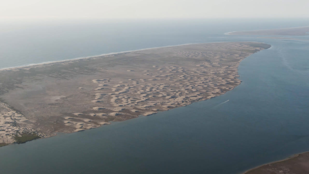 Wide aerial coastline with sand formations and calm water.